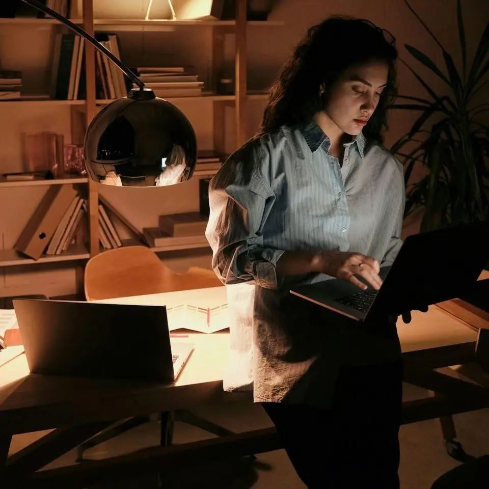 Dans notre bureau d'étude à notre atelier femme travaillant sur un ordinateur portable dans un environnement sombre et moderne - Etude de projet et devis